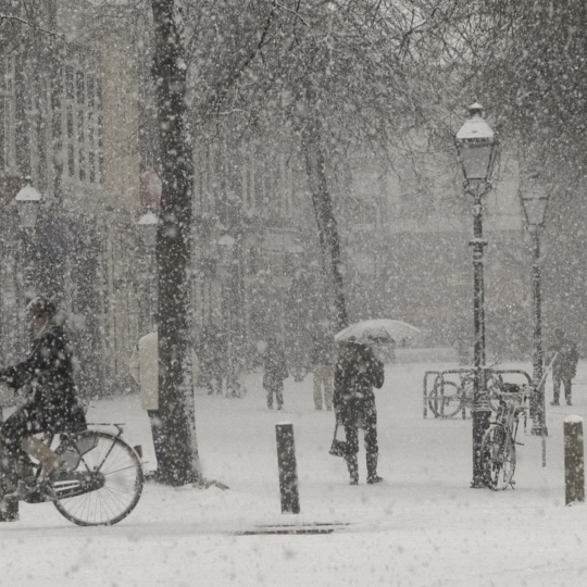 Eine Fußgängerzone, mit fallendem Schnee und Menschen, die unterwegs sind.