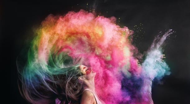 Eine Frau wirft ihren Kopf nach hinten, während Farbpulver aus ihren Haaren in die Luft wirbelt.