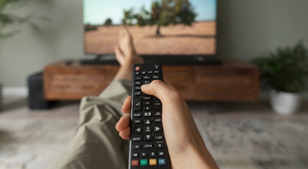 Eine Hand hält eine Fernbedingung in Richtung Fernseher.