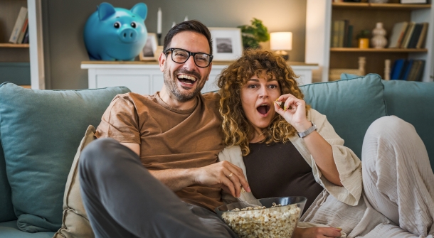 Zwei Menschen auf einer Couch die lachen und Popcorn essen.